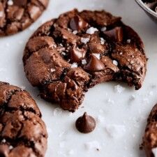 chocolate cookies with sea salt on top and one broken in half, sitting on a white surface