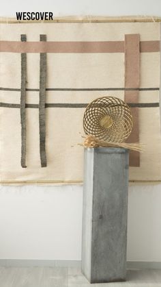 a tall vase sitting in front of a wall hanging on a wall next to a metal container