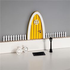 a white table with a yellow door and some keys on top of it, in front of a gray wall