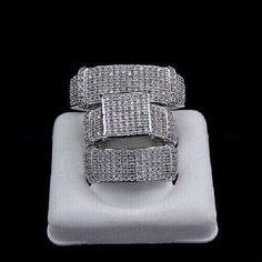 two white gold and diamond rings sitting on top of a white square plate in front of a black background