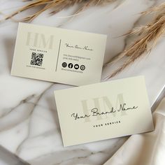 two business cards sitting on top of a marble table next to some dried grass and flowers