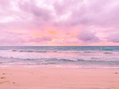 the beach has waves coming in from the ocean and pink clouds over the blue water