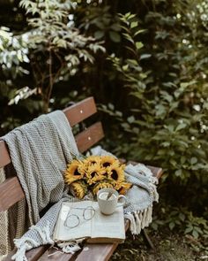 a wooden bench with a book, coffee cup and sunflowers sitting on it