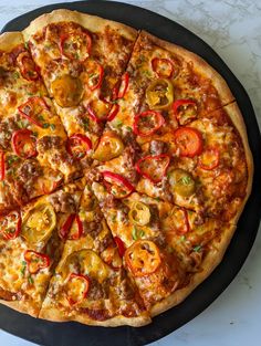 a pizza with many toppings sitting on top of a black plate next to a white counter