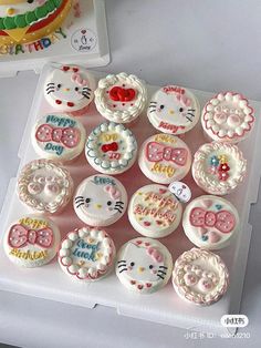 hello kitty cupcakes are displayed on a white tray next to a birthday cake