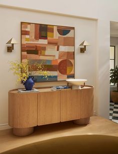 a living room with a painting on the wall next to a wooden cabinet and vase