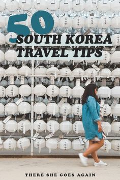 there is a woman walking past a wall with white bags on it and the words 50 south korea travel tips