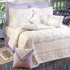 a bed with purple and white bedspread, pillows and rugs on brick patio