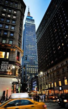 a taxi cab driving down a street next to tall buildings in new york city at night