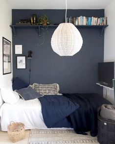 a bedroom with a bed, bookshelf and hanging lamp in the corner between two walls