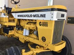 the front end of a yellow and black tractor parked in front of a garage door