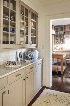 a kitchen with white cabinets and wooden floors is seen from the hallway to the dining room