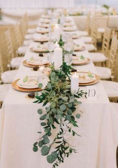 a long table with white linens and greenery is set for an elegant dinner