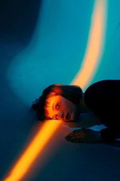 a woman laying on the ground in front of a blue wall with light coming from it