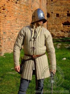 a man dressed in medieval clothing standing next to a brick wall with a helmet on