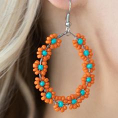 a close up of a person wearing large orange and turquoise beaded hoops earrings