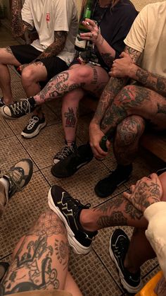 a group of men sitting next to each other with tattoos on their arms and legs