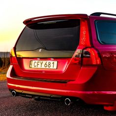 the back end of a red car parked on top of a parking lot at sunset