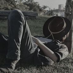 a man laying in the grass with his hat on top of his head, next to a tree