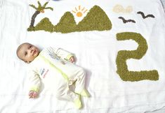 a baby laying on top of a white blanket next to numbers made out of grass