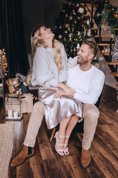 a man and woman sitting on a chair in front of a christmas tree, laughing