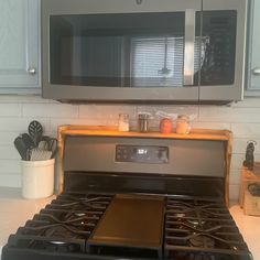 a stove with a microwave above it in a kitchen next to some utensils