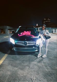 a woman standing next to a car with a pink bow on it