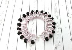 a black and pink bracelet on a white wooden floor with beads hanging from it's center