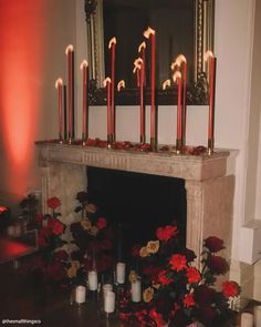 a fireplace with candles and flowers in front of the mantel decorated with red roses