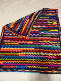 a multicolored crocheted blanket laying on top of a white bed sheet