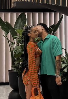 a man and woman standing next to each other in front of a plant filled wall