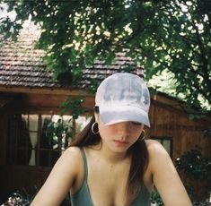 a young woman wearing a white hat sitting in front of a wooden building with trees