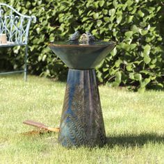 two birds sitting on top of a bird bath in the grass