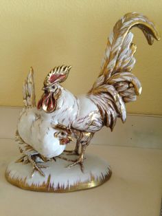 a white and gold rooster figurine sitting on top of a table next to a yellow wall