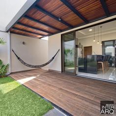 a hammock hanging from the side of a house next to a patio with grass