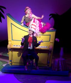 two people dressed as clowns sit on a piano in front of a purple background