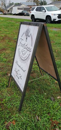 a sign sitting in the grass next to a car parked on top of a field