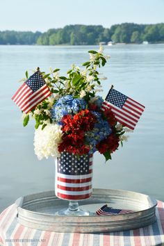 an american flag vase with flowers in it on top of a table near the water