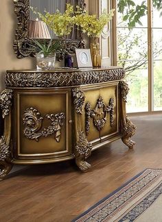 an ornately decorated gold sideboard stands in front of a large mirror and vase with flowers