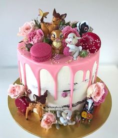 a cake with pink frosting and lots of little animals on top, sitting on a gold plate