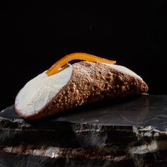 a piece of bread sitting on top of a black stone slab with an orange peel sticking out of it