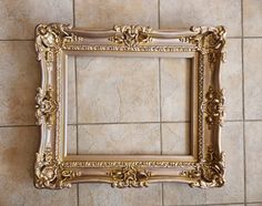 an ornate gold frame hanging on the wall in a tiled room with tile flooring