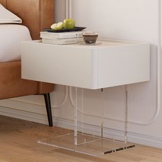 a white table with a bowl of fruit on top of it next to a bed