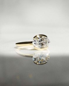 a yellow gold engagement ring with an oval cut diamond in the center on a reflective surface