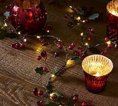 three red glass votives with christmas lights around them on a wooden table top