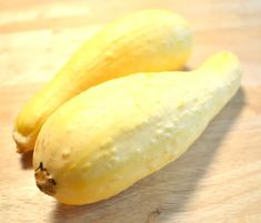 two yellow zucchini sitting on top of a wooden table