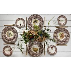 an arrangement of plates and flowers on a white wooden tablecloth with gold trimmings