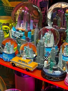 there are many snow globes on display in the store window with cars and buildings behind them