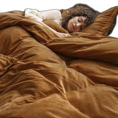 a woman laying in bed with her head on the pillow and she is covered by a brown blanket