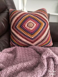 a crocheted pillow sitting on top of a couch next to a purple blanket